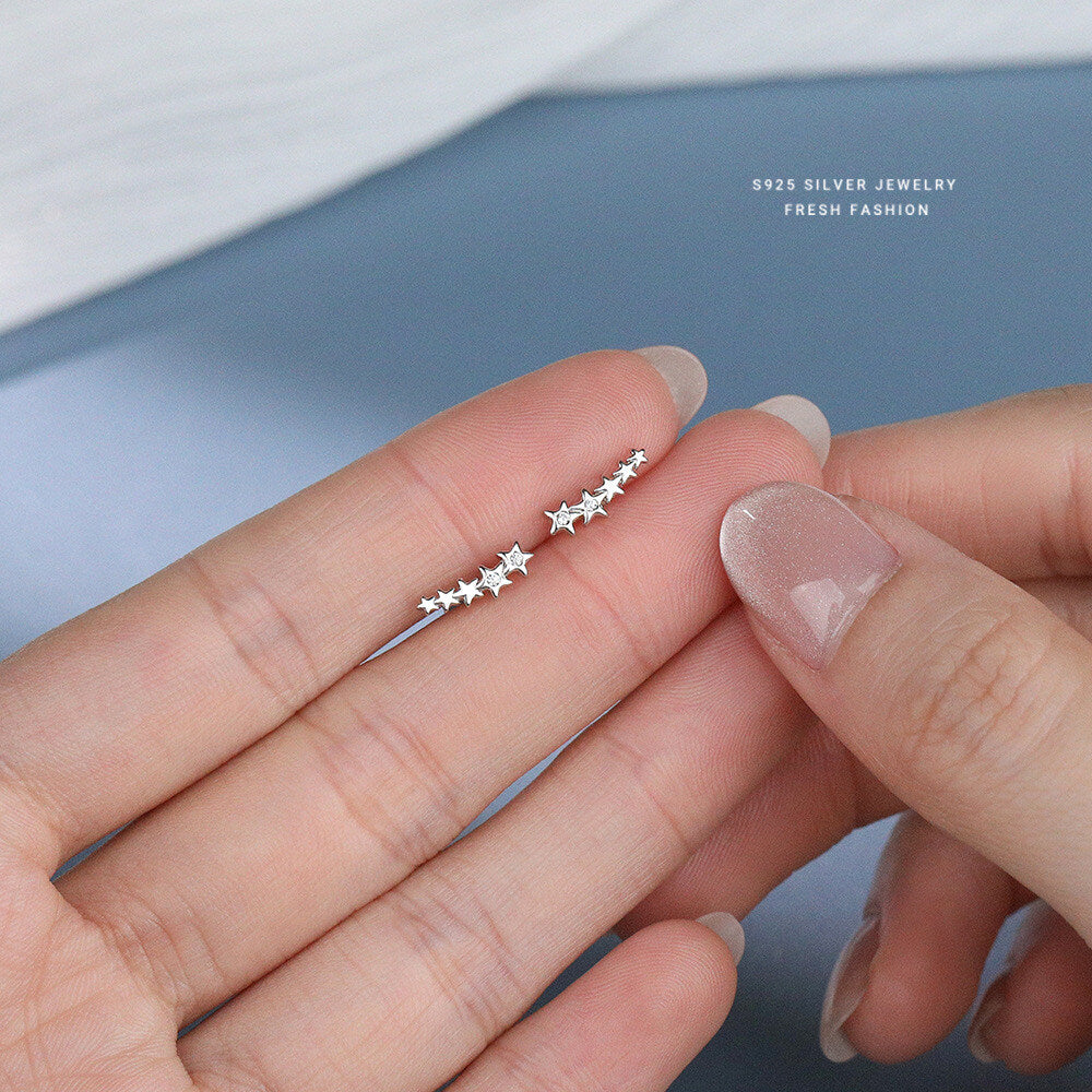 Top-down lifestyle shot of S925 sterling silver star climbers held between fingers showing clear cubic zirconia details