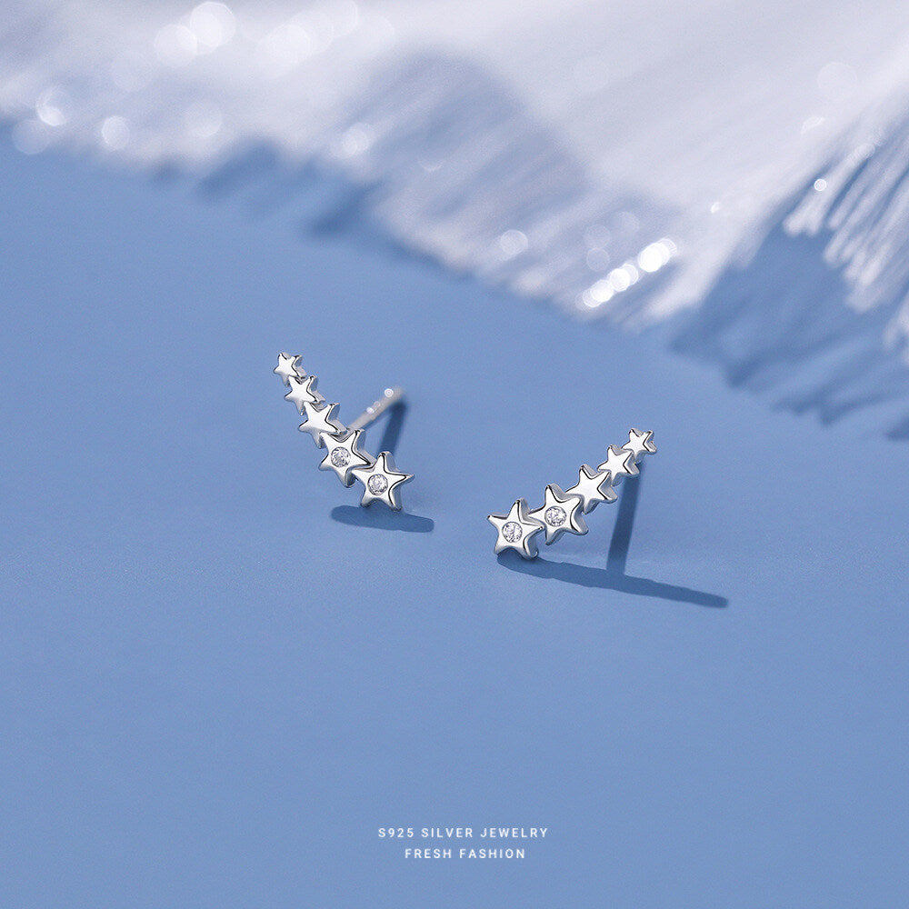 Pair of sterling silver star climber stud earrings on a minimalist matte-blue background