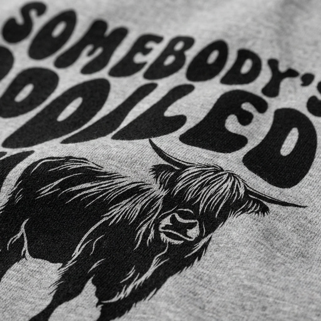 A close-up detail shot of the soft cotton texture and black graphic print on the Highland Cow Spoiled Farm Wife t-shirt